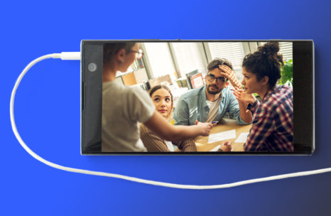 Image of cell phone with earbud cord attached. An image of 4 individuals around a table appears on the phone.